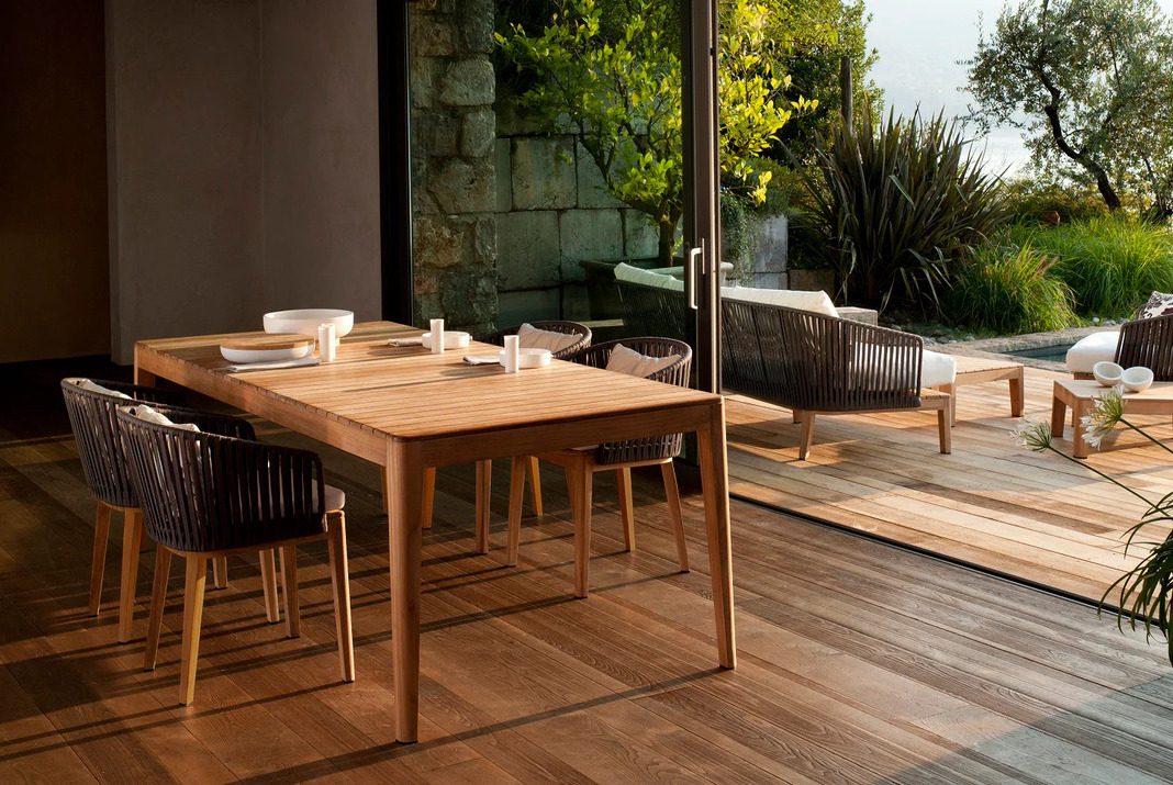 Teak dining table and chairs next to a window open to a terrace