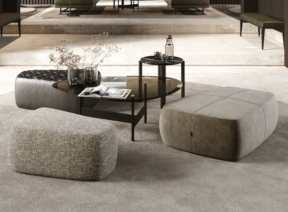 A lobby with different fabric textures in three separate puffs, a coffee table in smoked glass and dark metal, and a stone floor in a neutral interior material layering.